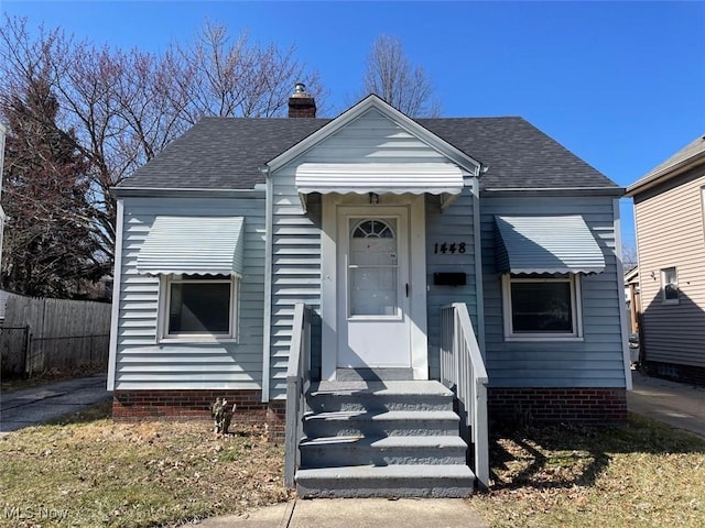 view of front of property with roof with shingles, a chimney, and fence