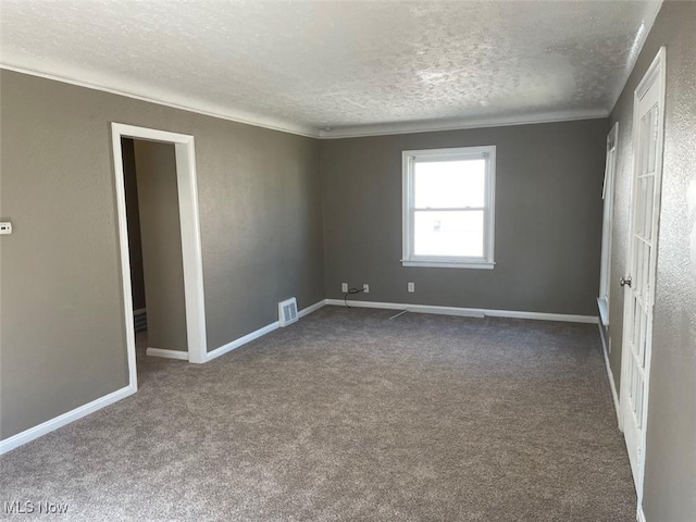 spare room featuring visible vents, ornamental molding, a textured ceiling, dark colored carpet, and baseboards