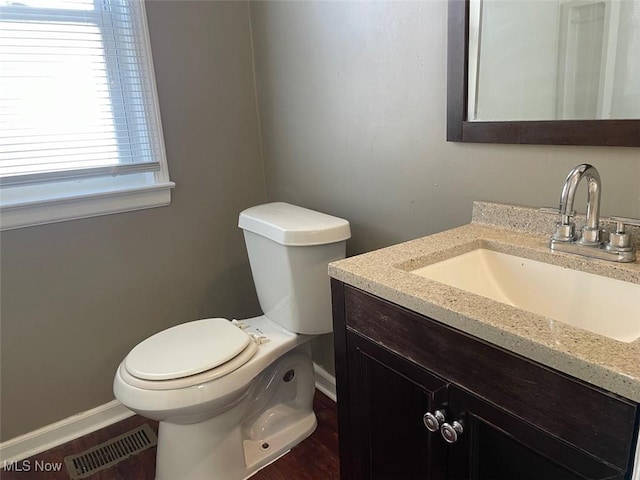 bathroom featuring visible vents, baseboards, toilet, wood finished floors, and vanity