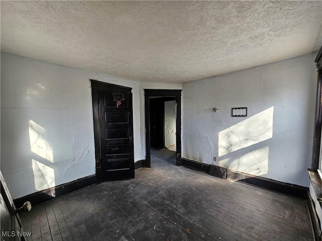 spare room with a textured ceiling, baseboards, and hardwood / wood-style floors