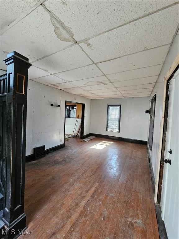 empty room featuring hardwood / wood-style flooring, a paneled ceiling, and baseboards