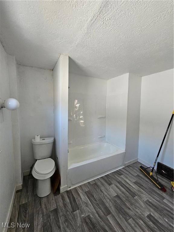 full bath featuring a textured ceiling, toilet, bathing tub / shower combination, and wood finished floors