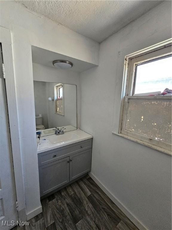 bathroom featuring toilet, a textured ceiling, wood finished floors, baseboards, and vanity