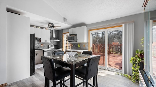 dining room with lofted ceiling, a textured ceiling, light wood-style flooring, and a ceiling fan