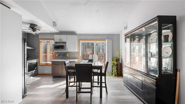 dining room featuring a ceiling fan, light wood-style floors, and a textured ceiling