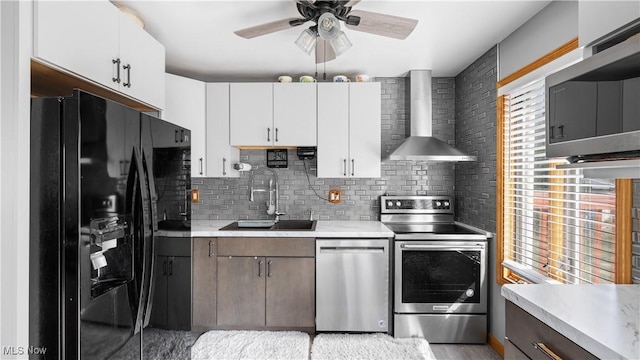 kitchen with a ceiling fan, a sink, appliances with stainless steel finishes, wall chimney exhaust hood, and light countertops