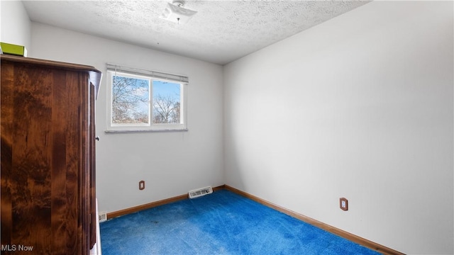 carpeted empty room featuring baseboards, visible vents, and a textured ceiling