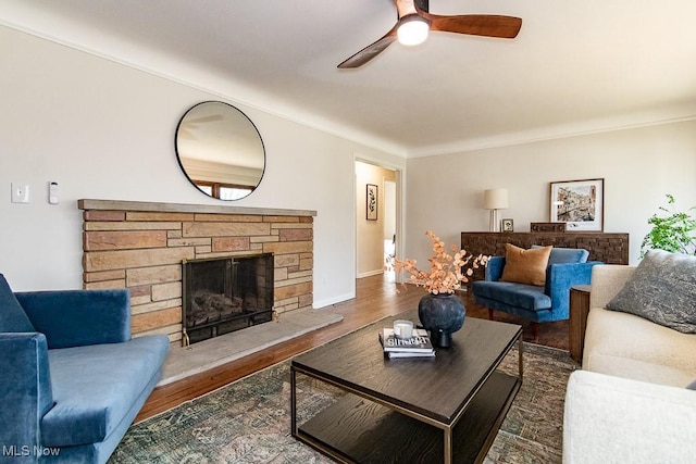 living area featuring a fireplace, baseboards, ceiling fan, and wood finished floors