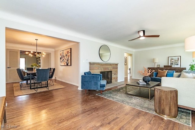 living room featuring a stone fireplace, ceiling fan with notable chandelier, wood finished floors, and baseboards