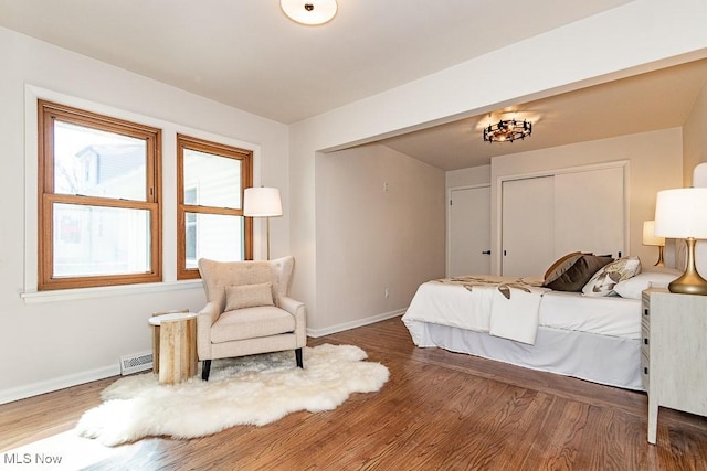 bedroom with a closet, visible vents, baseboards, and wood finished floors