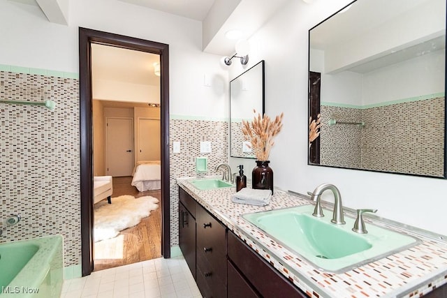 full bath featuring double vanity, tile walls, ensuite bathroom, and a sink