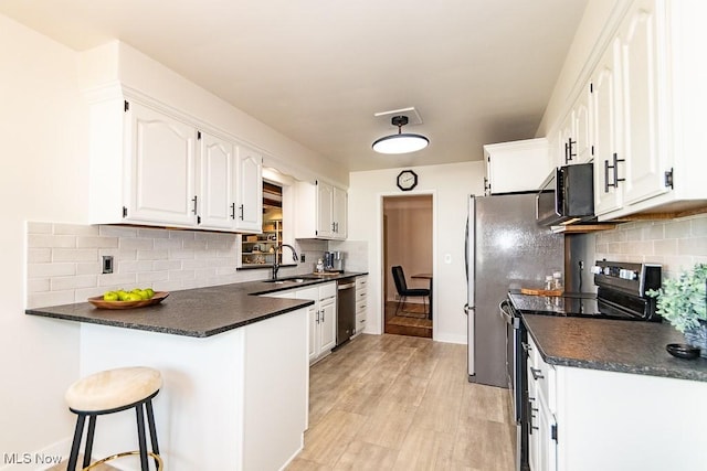 kitchen with a sink, dark countertops, appliances with stainless steel finishes, a peninsula, and white cabinets