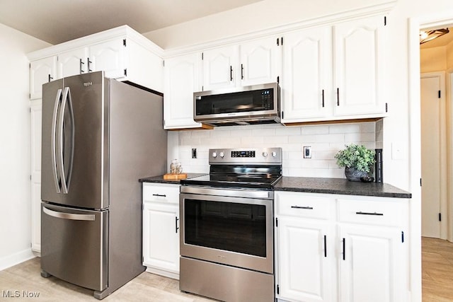 kitchen with dark countertops, white cabinetry, stainless steel appliances, light wood finished floors, and decorative backsplash