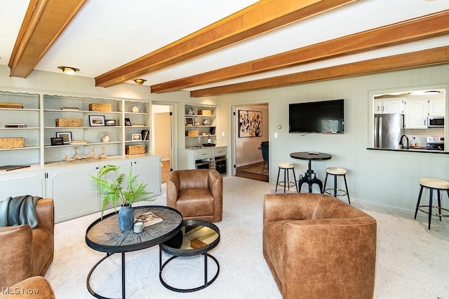 living area with beamed ceiling, light carpet, and baseboards