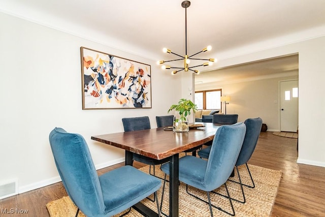 dining space featuring a notable chandelier, baseboards, visible vents, and wood finished floors