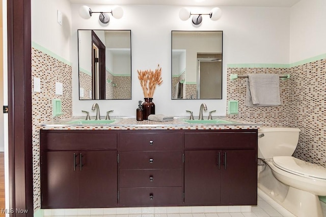 bathroom featuring double vanity, a sink, a shower stall, tile walls, and toilet