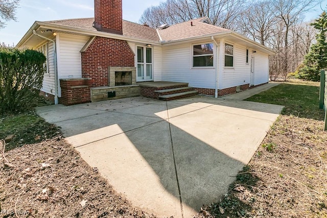 rear view of house with a patio, roof with shingles, and a chimney