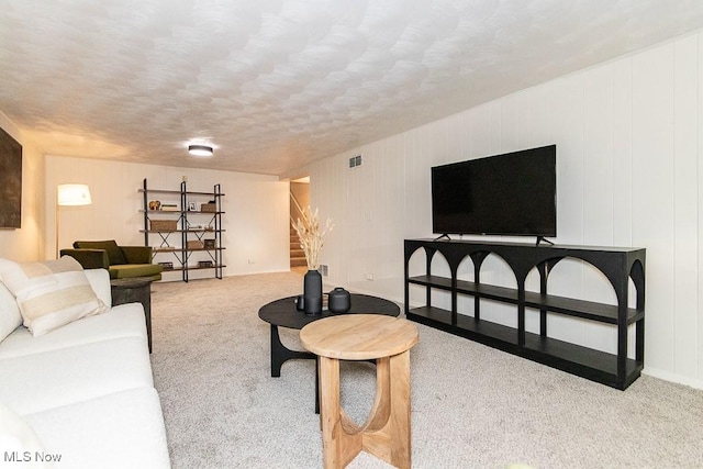 carpeted living room featuring stairway, a textured ceiling, and visible vents