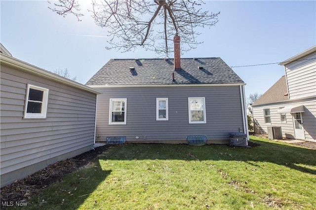 back of property with a chimney, cooling unit, a shingled roof, and a yard