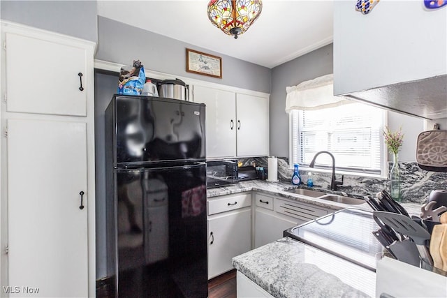 kitchen featuring a sink, light stone countertops, freestanding refrigerator, white cabinets, and dark wood-style flooring