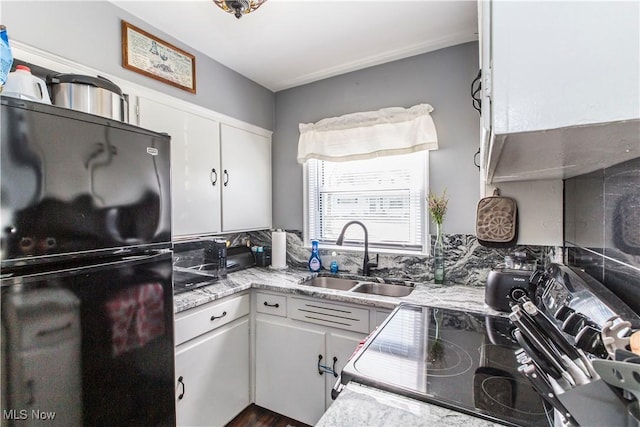 kitchen with a sink, light stone counters, white cabinets, and freestanding refrigerator