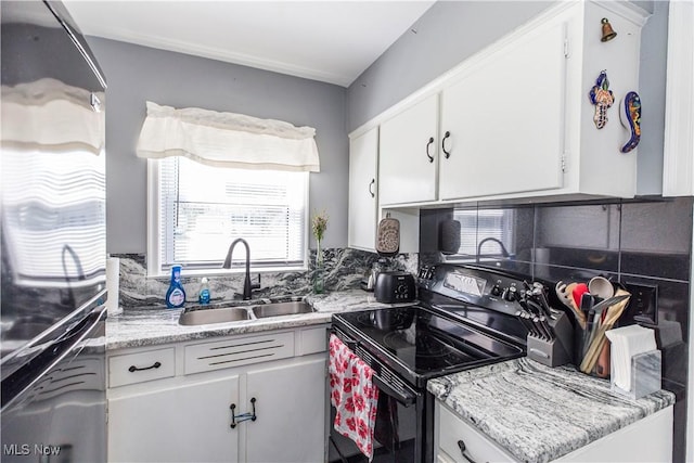 kitchen featuring black range with electric stovetop, decorative backsplash, freestanding refrigerator, white cabinets, and a sink