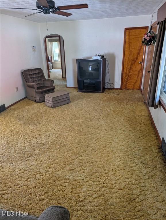 unfurnished living room with a ceiling fan, carpet flooring, baseboards, and arched walkways