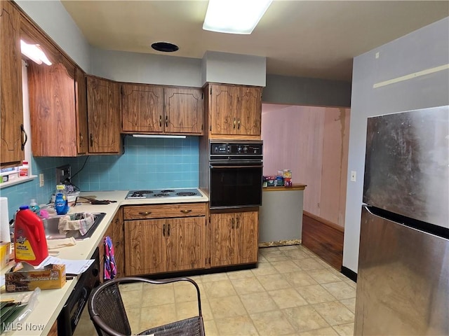 kitchen featuring oven, electric cooktop, light countertops, and freestanding refrigerator