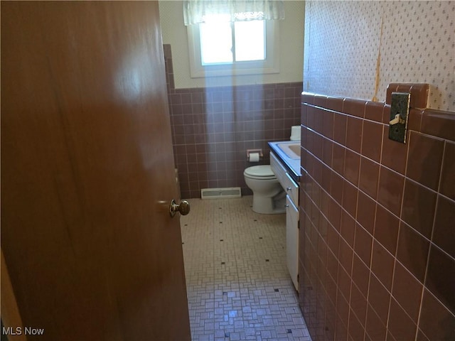 bathroom with visible vents, tile walls, toilet, tile patterned floors, and vanity