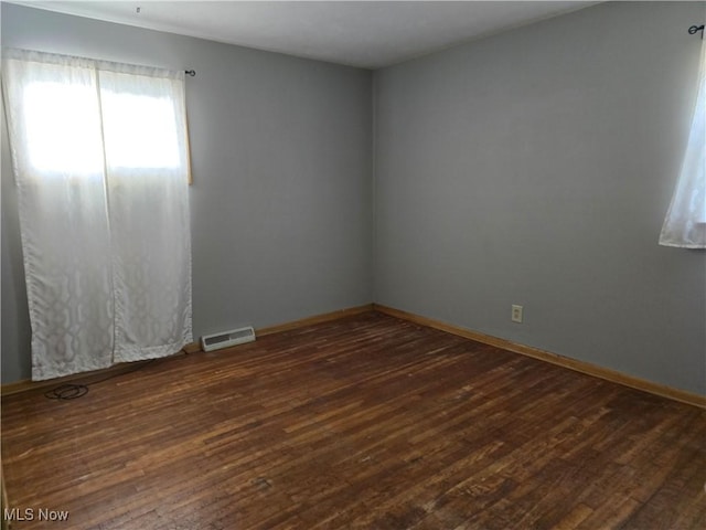 unfurnished room featuring visible vents, dark wood-type flooring, and baseboards