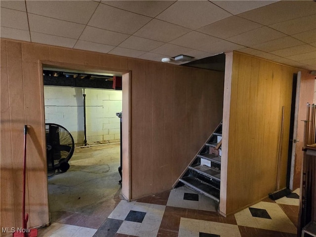 finished below grade area featuring tile patterned floors, stairway, a drop ceiling, and wood walls