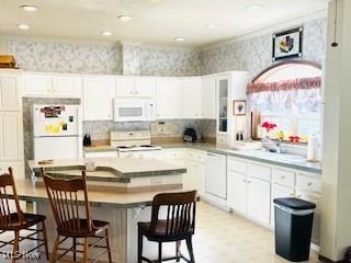 kitchen featuring white appliances, wallpapered walls, a breakfast bar, white cabinets, and a center island