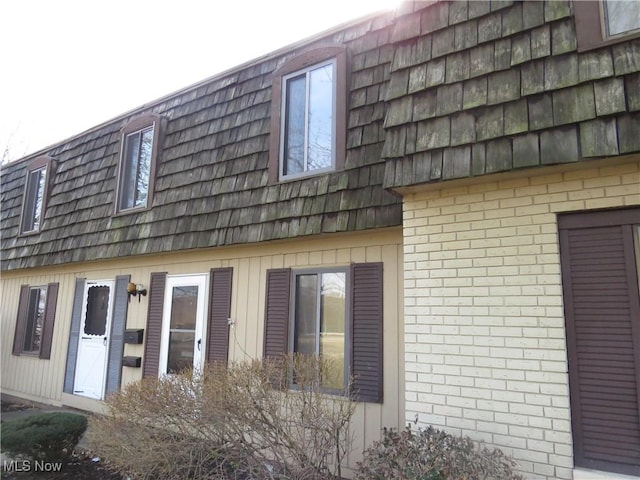 view of side of home featuring mansard roof and brick siding