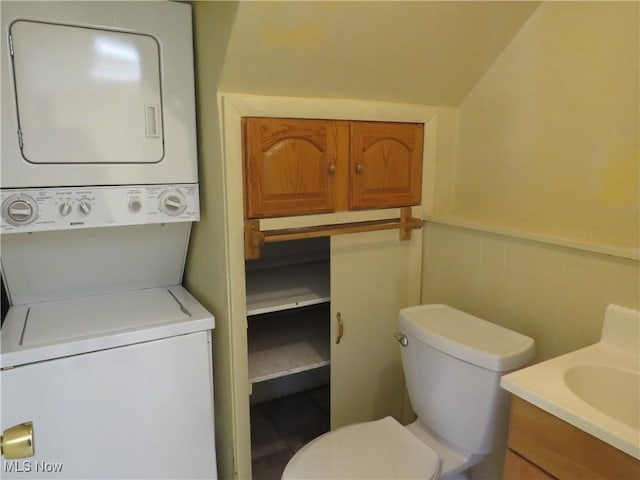 bathroom with vanity, stacked washer and dryer, toilet, and wainscoting