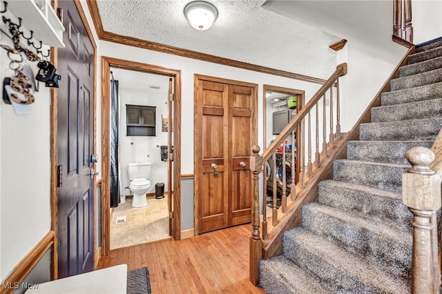 stairs with hardwood / wood-style floors, a textured ceiling, and ornamental molding