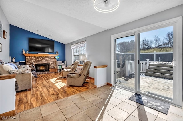 living area with tile patterned floors, lofted ceiling, a textured ceiling, baseboards, and a brick fireplace