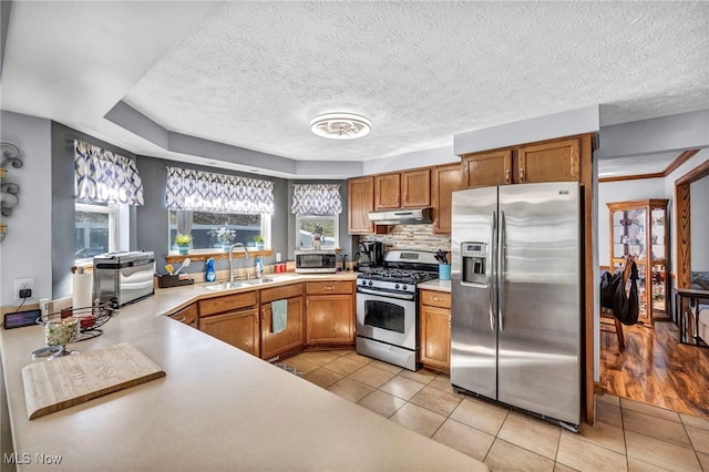 kitchen featuring under cabinet range hood, appliances with stainless steel finishes, light countertops, and a sink