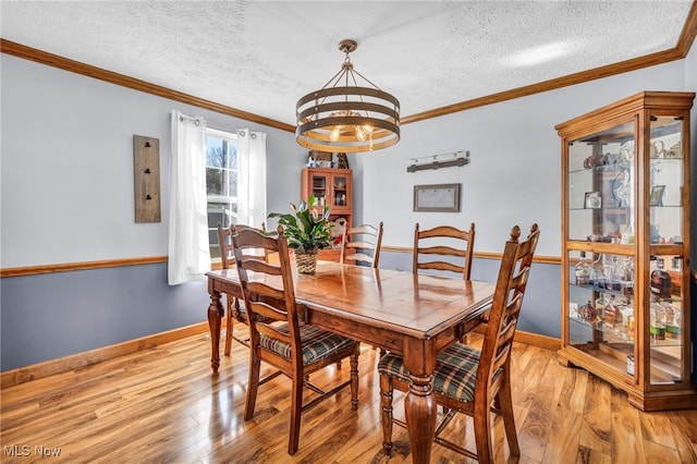 dining room featuring baseboards, light wood-style flooring, a textured ceiling, crown molding, and a chandelier