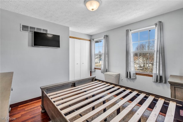 unfurnished bedroom with visible vents, baseboards, wood finished floors, a closet, and a textured ceiling