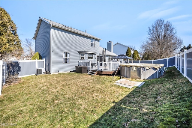 back of house featuring a deck, a fenced backyard, a fenced in pool, and a lawn