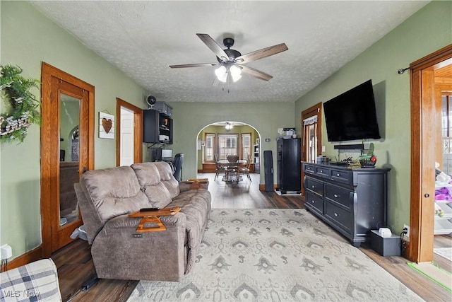 living room with arched walkways, a textured ceiling, ceiling fan, and wood finished floors