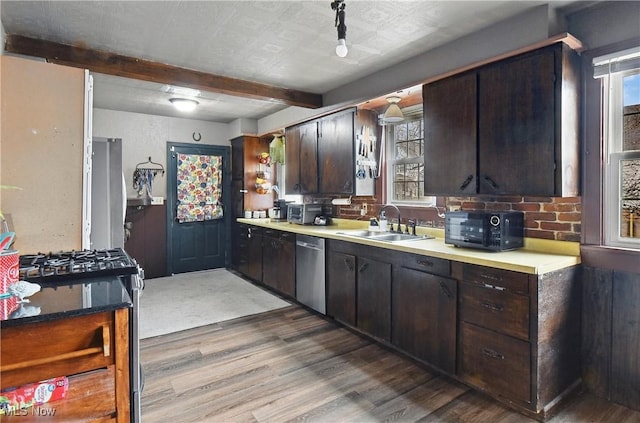 kitchen with wood finished floors, beam ceiling, a sink, light countertops, and appliances with stainless steel finishes