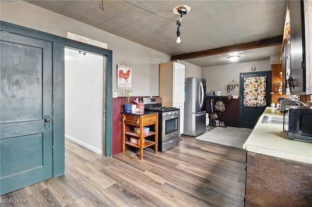 kitchen featuring beamed ceiling, appliances with stainless steel finishes, light countertops, and light wood-style floors