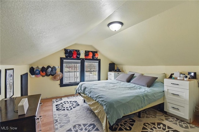 bedroom with vaulted ceiling, a textured ceiling, and wood finished floors