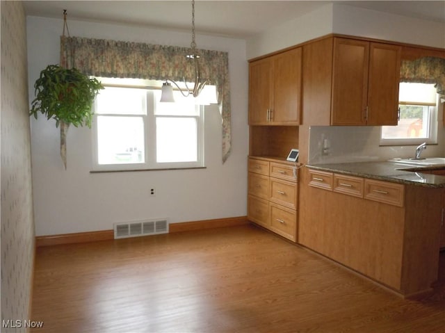 kitchen featuring tasteful backsplash, visible vents, baseboards, light wood-style flooring, and a sink