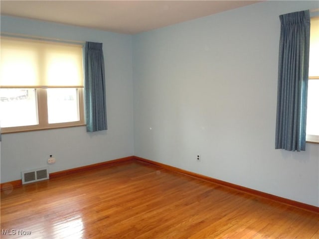 spare room featuring light wood finished floors, visible vents, and baseboards