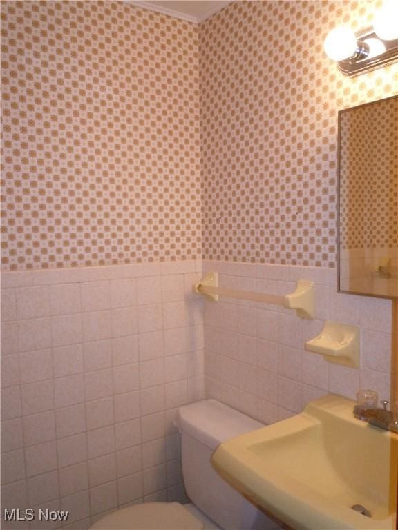 half bathroom with a sink, toilet, tile walls, and wallpapered walls