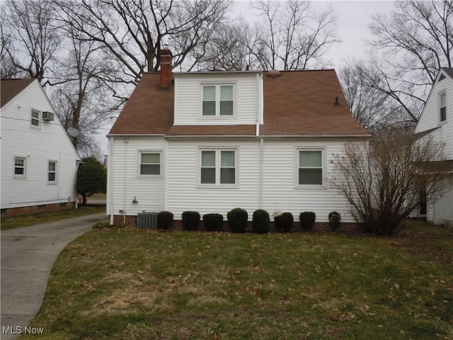 rear view of house with cooling unit, a chimney, a yard, and roof with shingles