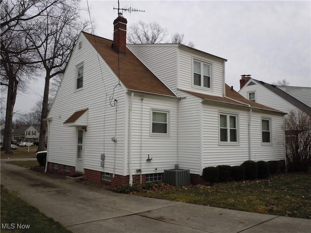 view of side of property featuring central air condition unit, roof with shingles, and a chimney