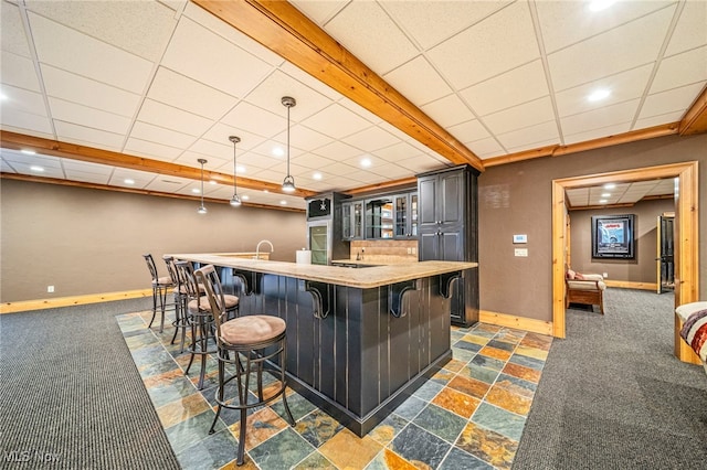 bar with indoor wet bar, a paneled ceiling, baseboards, and dark colored carpet